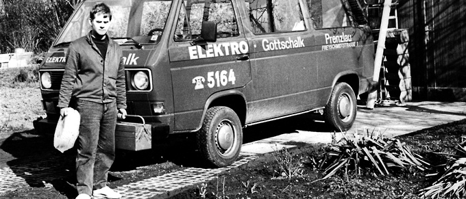 Ein Schwarzweiß-Foto vom Firmengründer vor einem alten Firmenbus